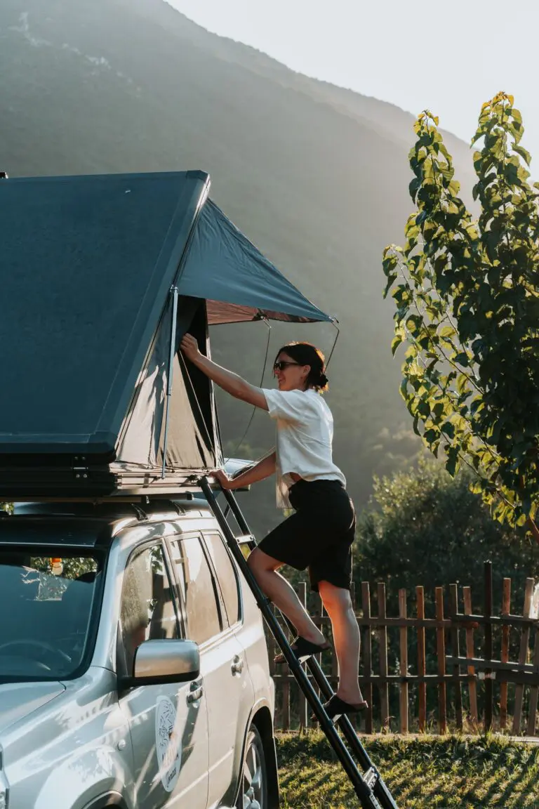 woman climbing ladder to rooftop tent on car in mountains