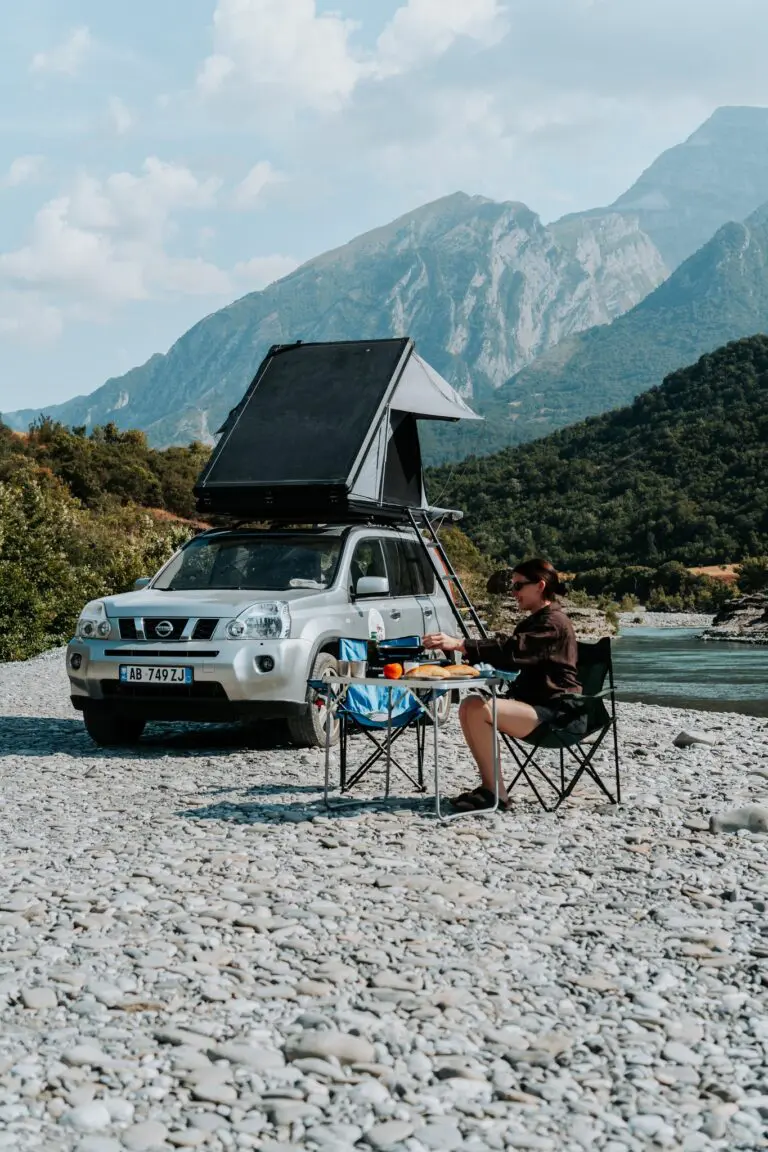 woman camping by river with rooftop tent car in Albania mountains