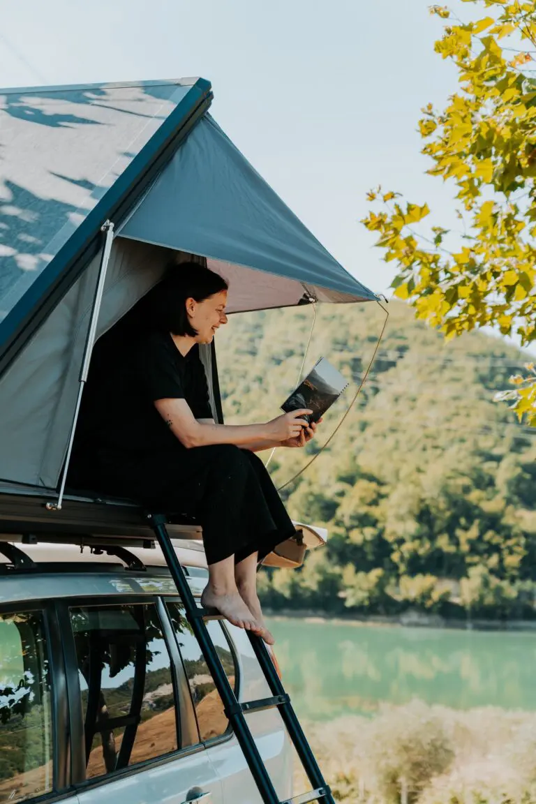 woman reading in rooftop tent by lake in Albania