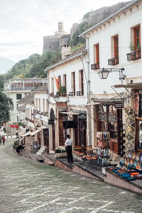 cobblestone street in Gjirokastra with shops and castle in background