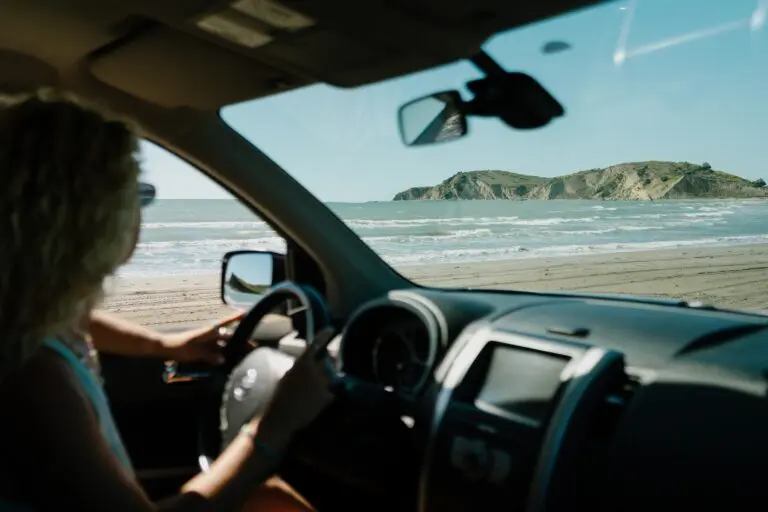 woman driving car on beach looking at sea and island