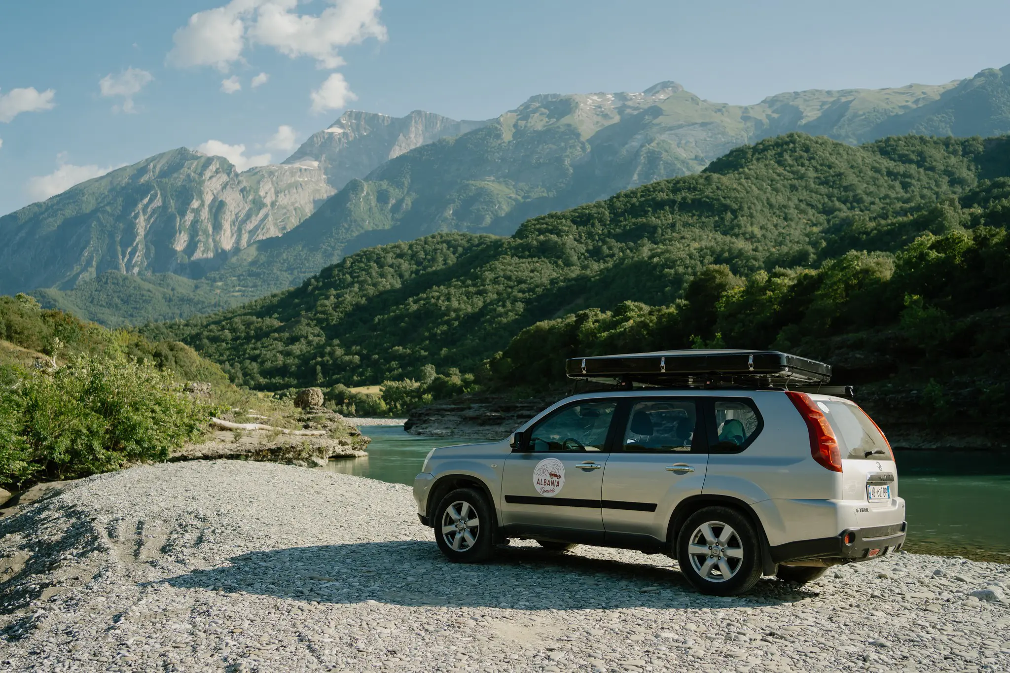 silver SUV with roof tent parked by a river in Albania