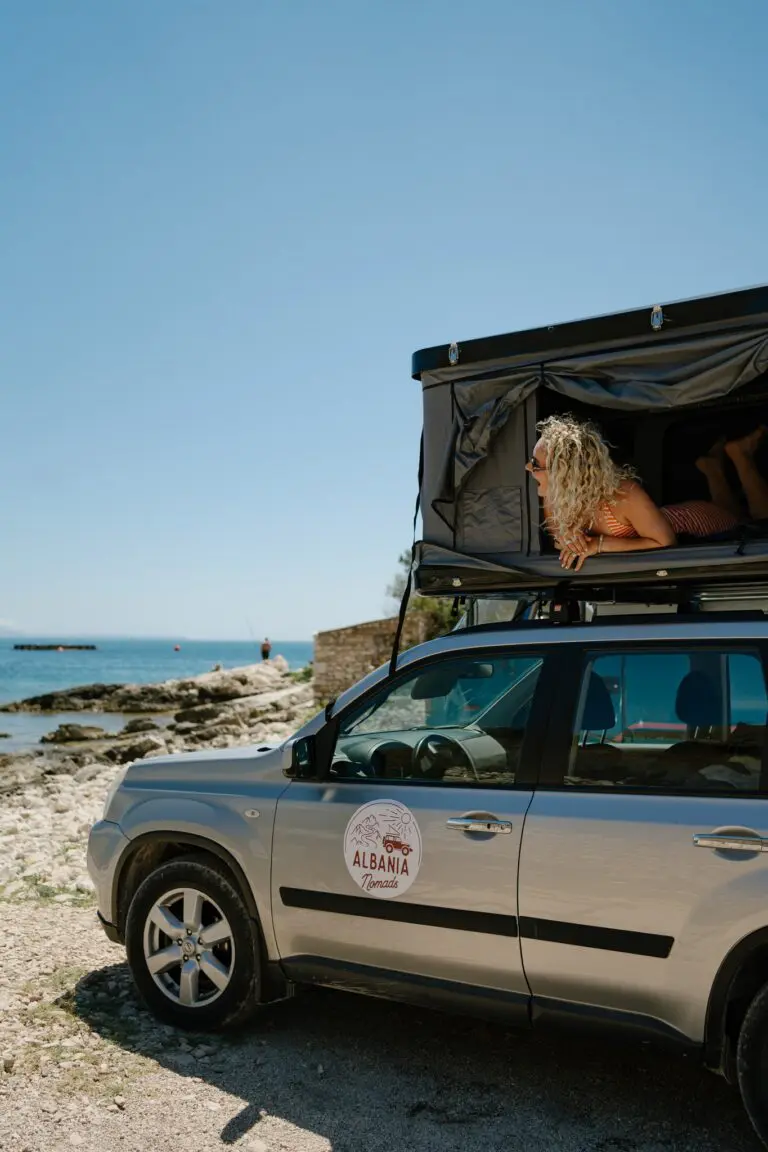 woman relaxing in rooftop tent by the sea in Porto Palermo