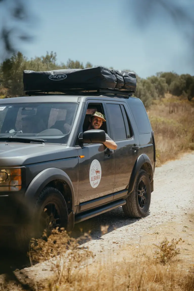 man smiling from car window on a dusty road in Albania