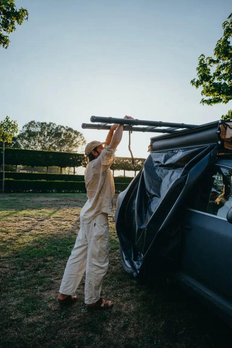 person setting up rooftop tent on car at sunset