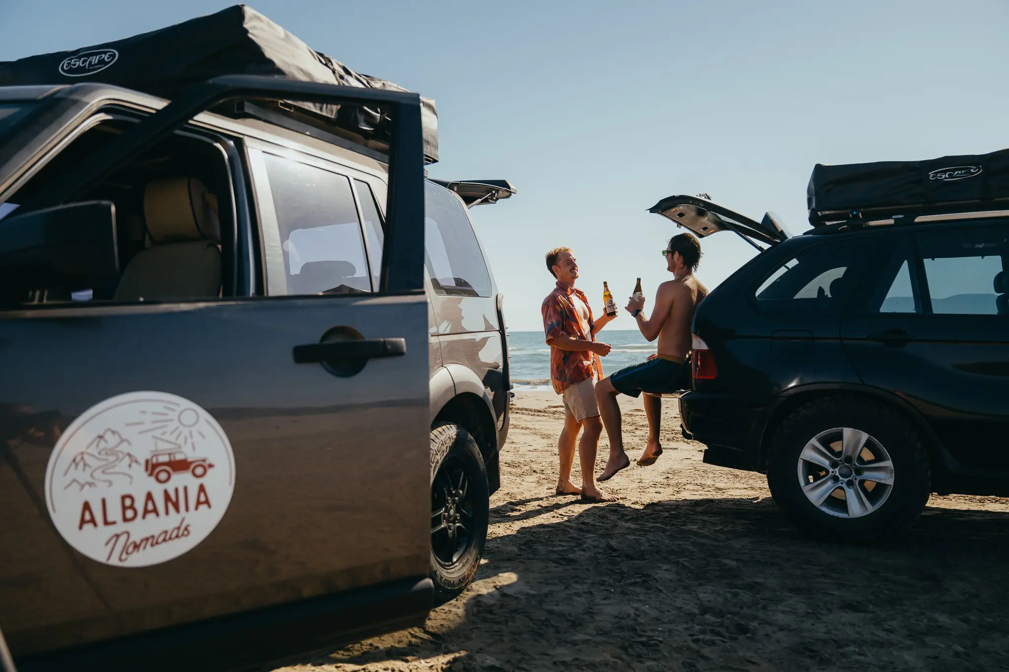 two men drinking beer by cars on beach in Albania