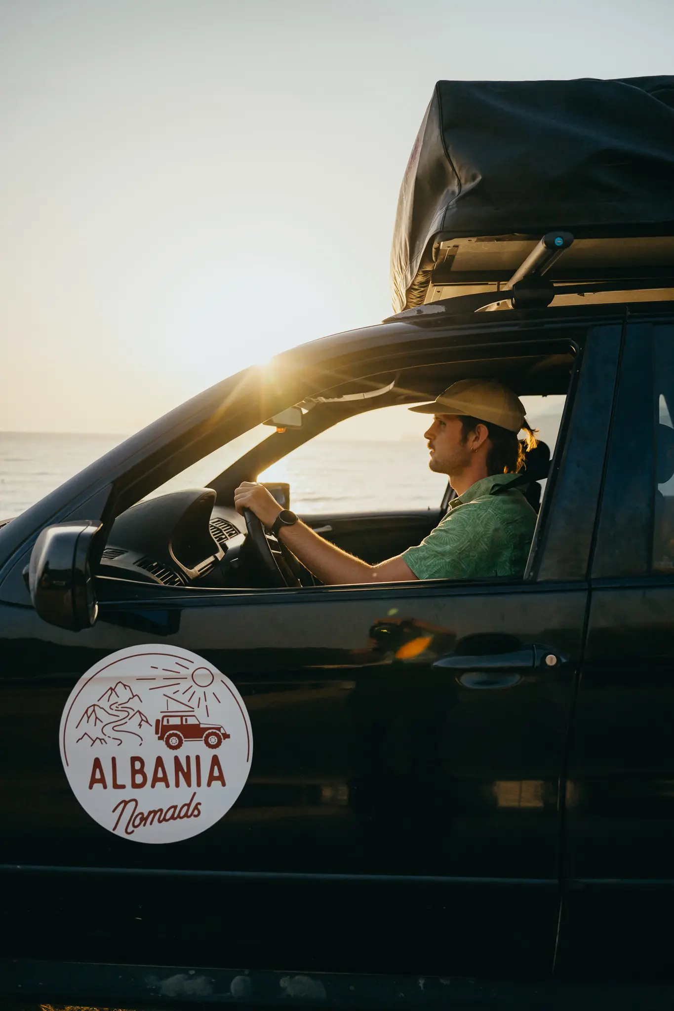 man driving a car with a rooftop tent at sunset by the sea