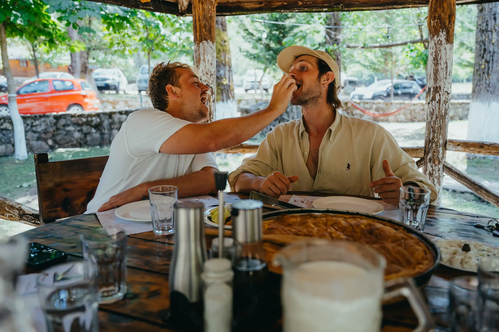 two men laughing and sharing food at an outdoor restaurant in Albania