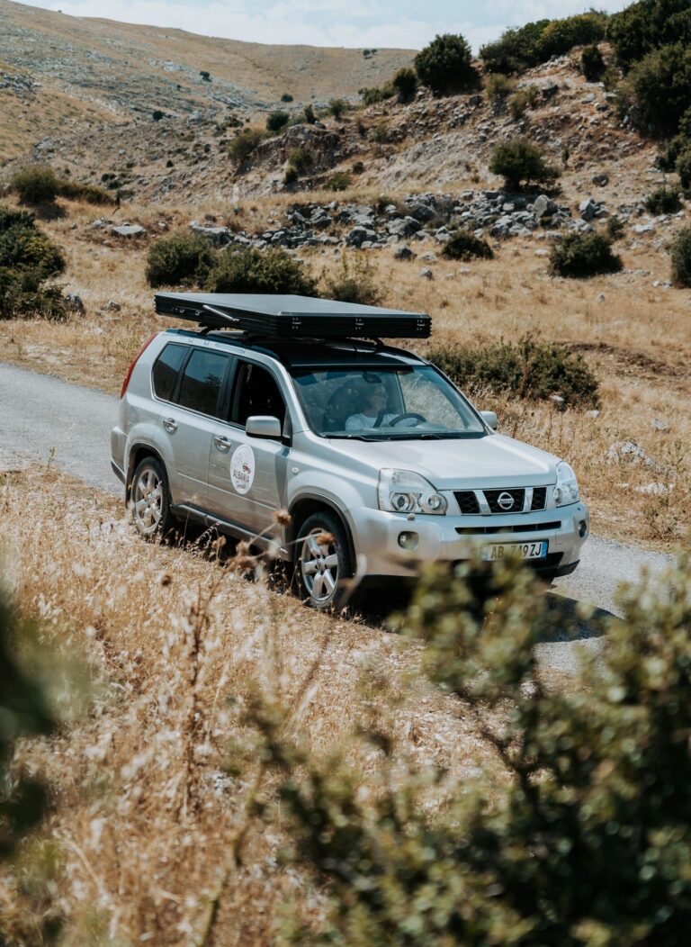 silver SUV with rooftop tent driving on a mountain road in Albania
