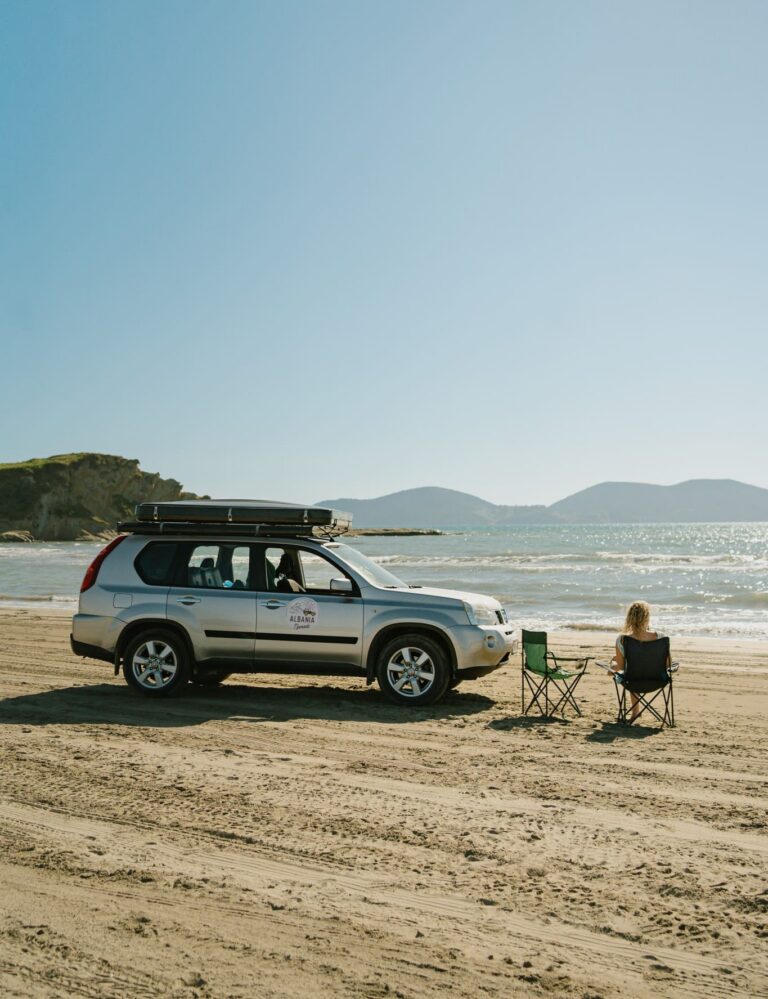 woman relaxing on beach next to car with rooftop tent in Albania