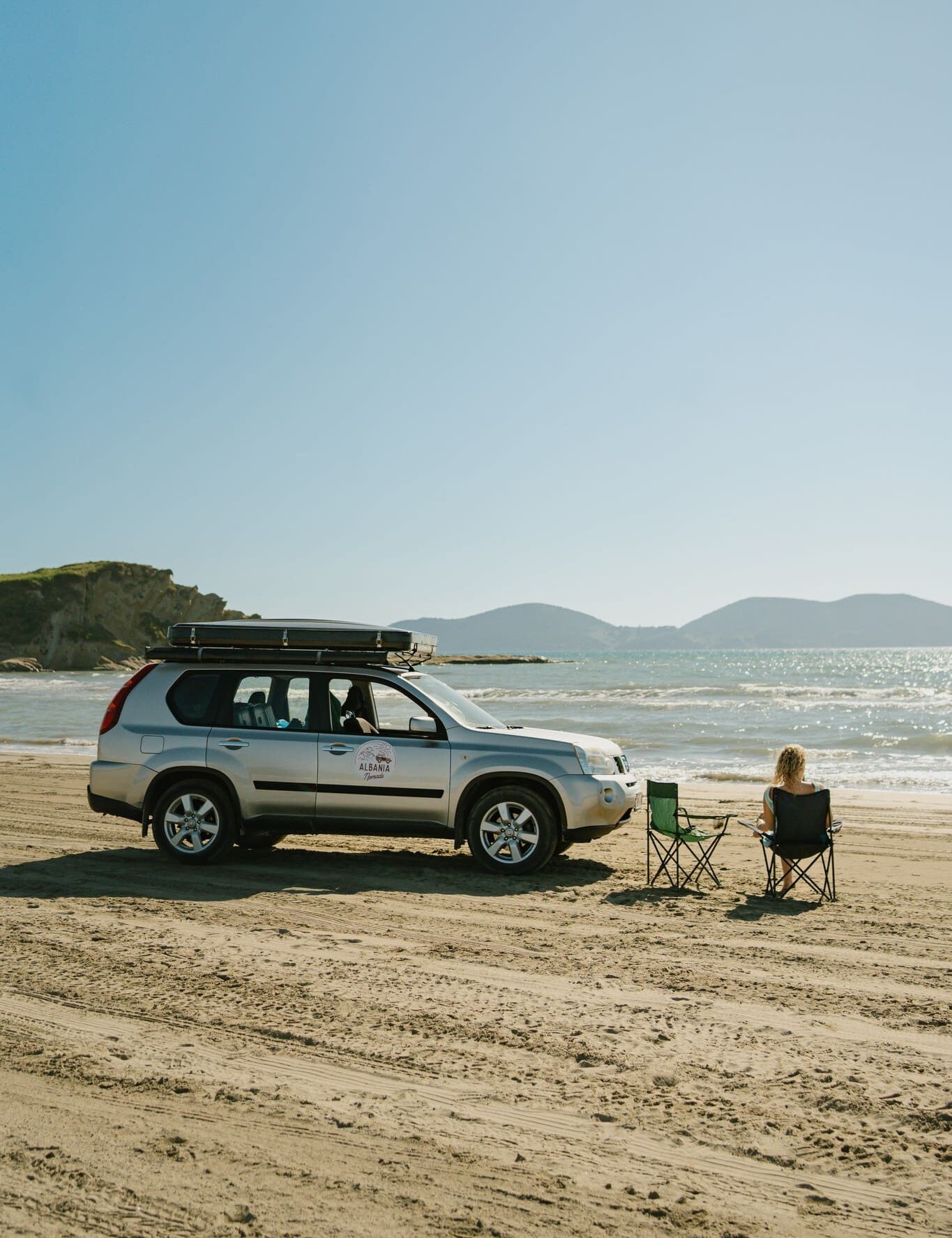 woman relaxing on beach next to car with rooftop tent in Albania