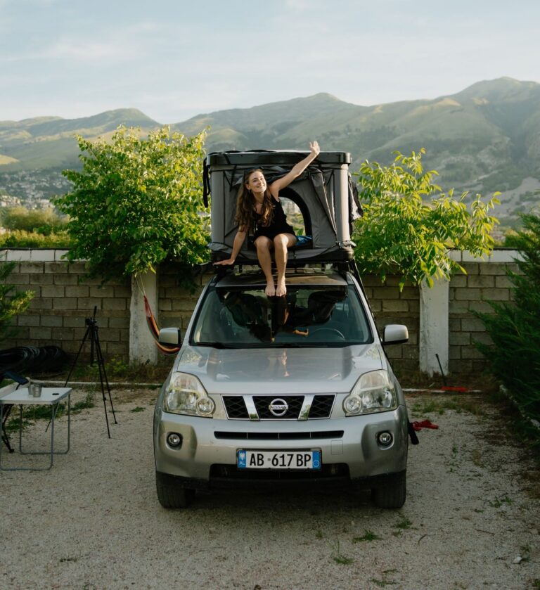 woman sitting on rooftop tent on car in mountains